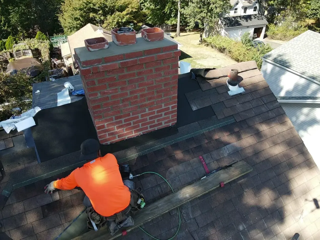 Roof repair in New Jersey: roofer setting new step flashing against a rebuilt brick chimney on a dark shingle roof