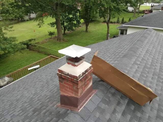 Rebuilt brick chimney with a new cap and brown flashing on a gray shingle roof