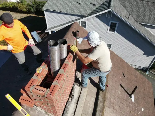 Two masons rebuilding a chimney crown around new clay flue liners