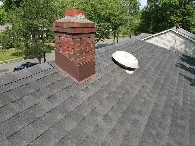 Finished brown flashing on a brick chimney and a new vent collar on gray shingles