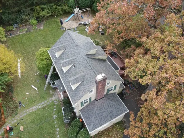 Finished gray shingle roof on a dormered New Jersey home surrounded by autumn trees