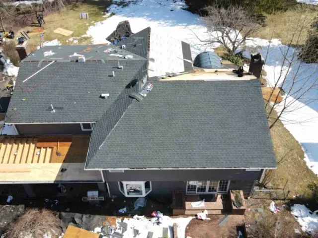 Aerial view of a winter roof repair with snow on the ground and a section of new shingles