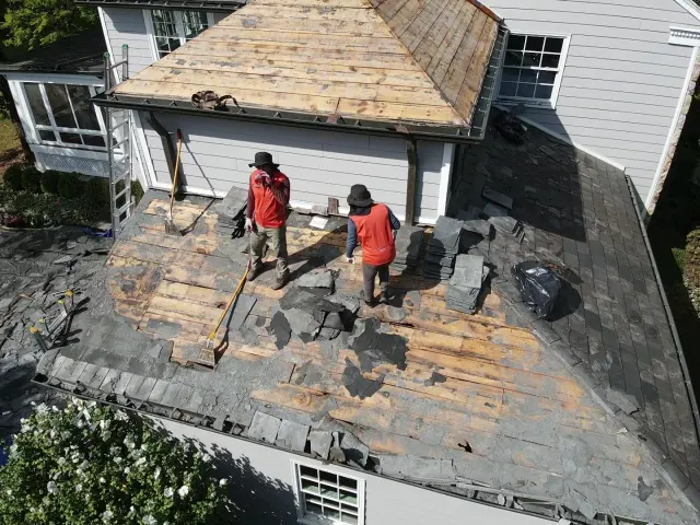 Two roofers on a small roof section stripped down to the wood deck