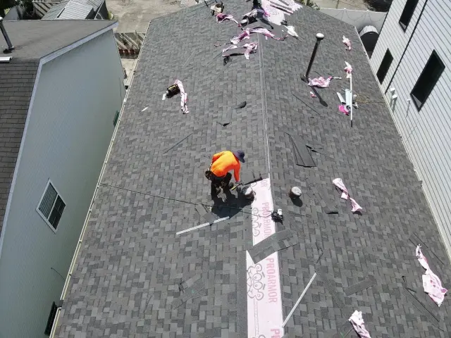 Shingle repair: roofer shingling a patch over a strip of fresh underlayment on a dark gray roof