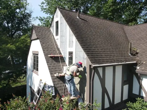 Roofer on a ladder checking the siding and roofline of a Tudor-style home