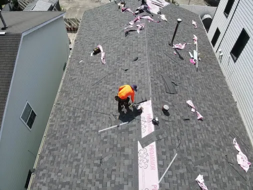 Crew member finishing a new gray shingle roof between two houses