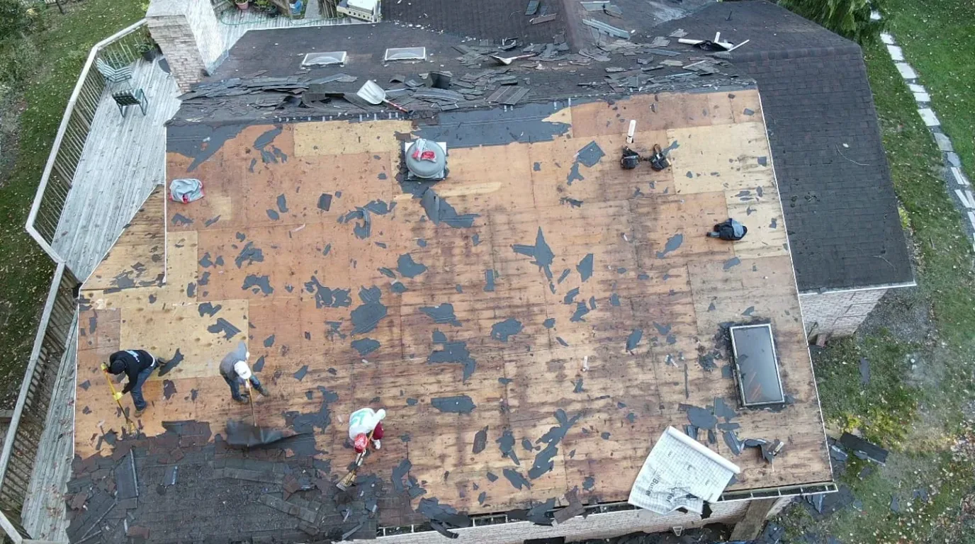 Roof replacement in New Jersey: crew stripping old shingles down to the plywood deck during a full tear-off